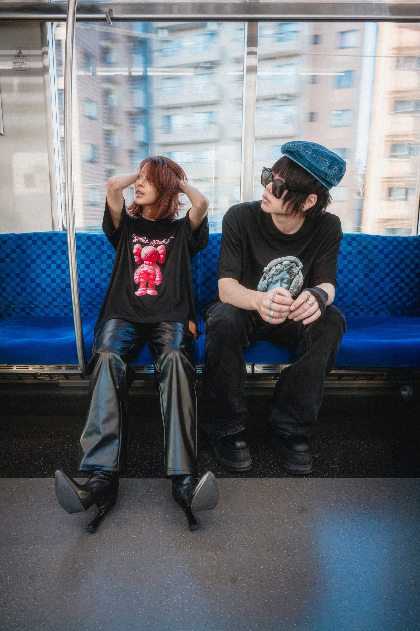 Two people sitting on a blue bench inside a train with cityscape outside
