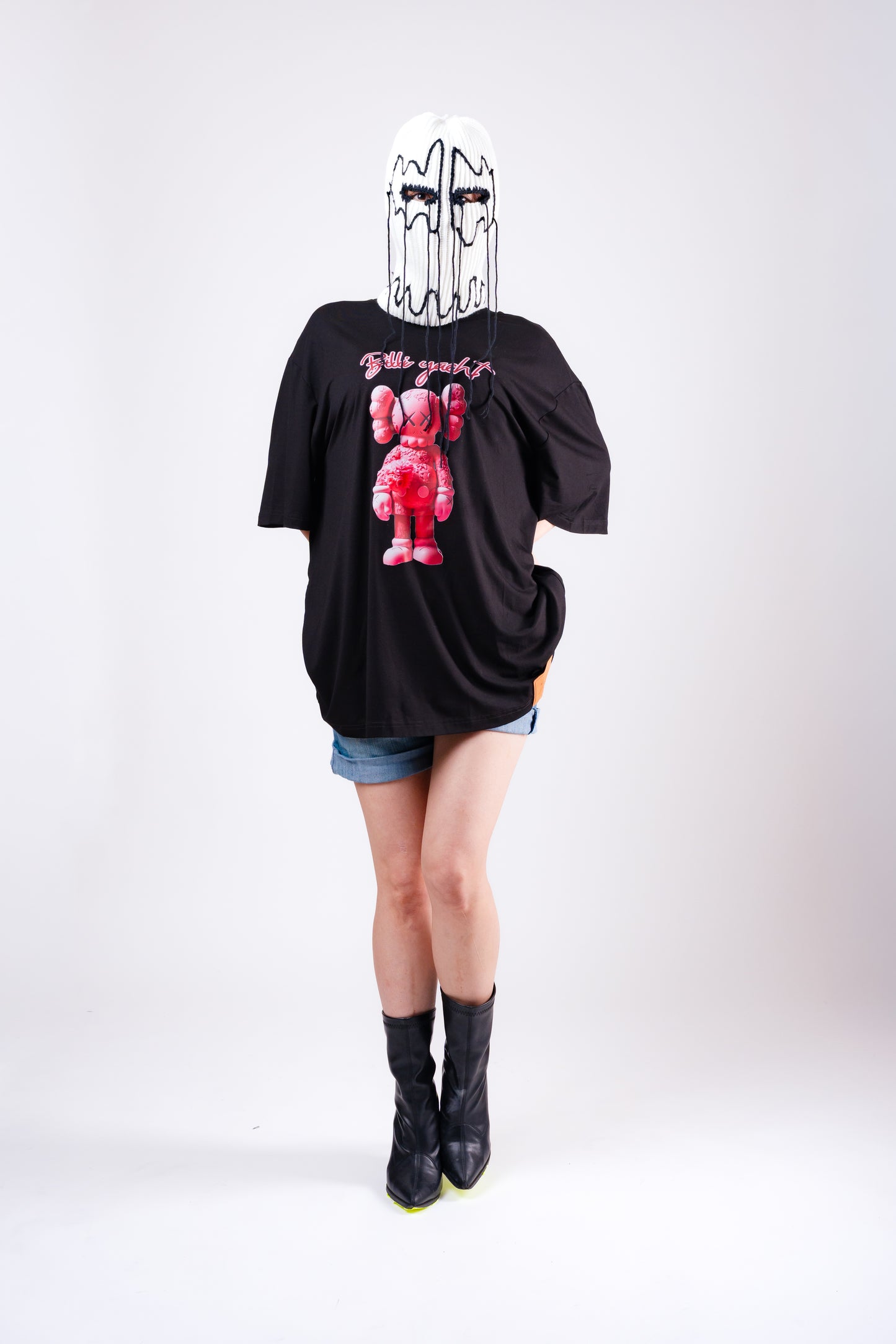 Person wearing a black t-shirt with a graphic design, denim shorts, and black boots on a white background