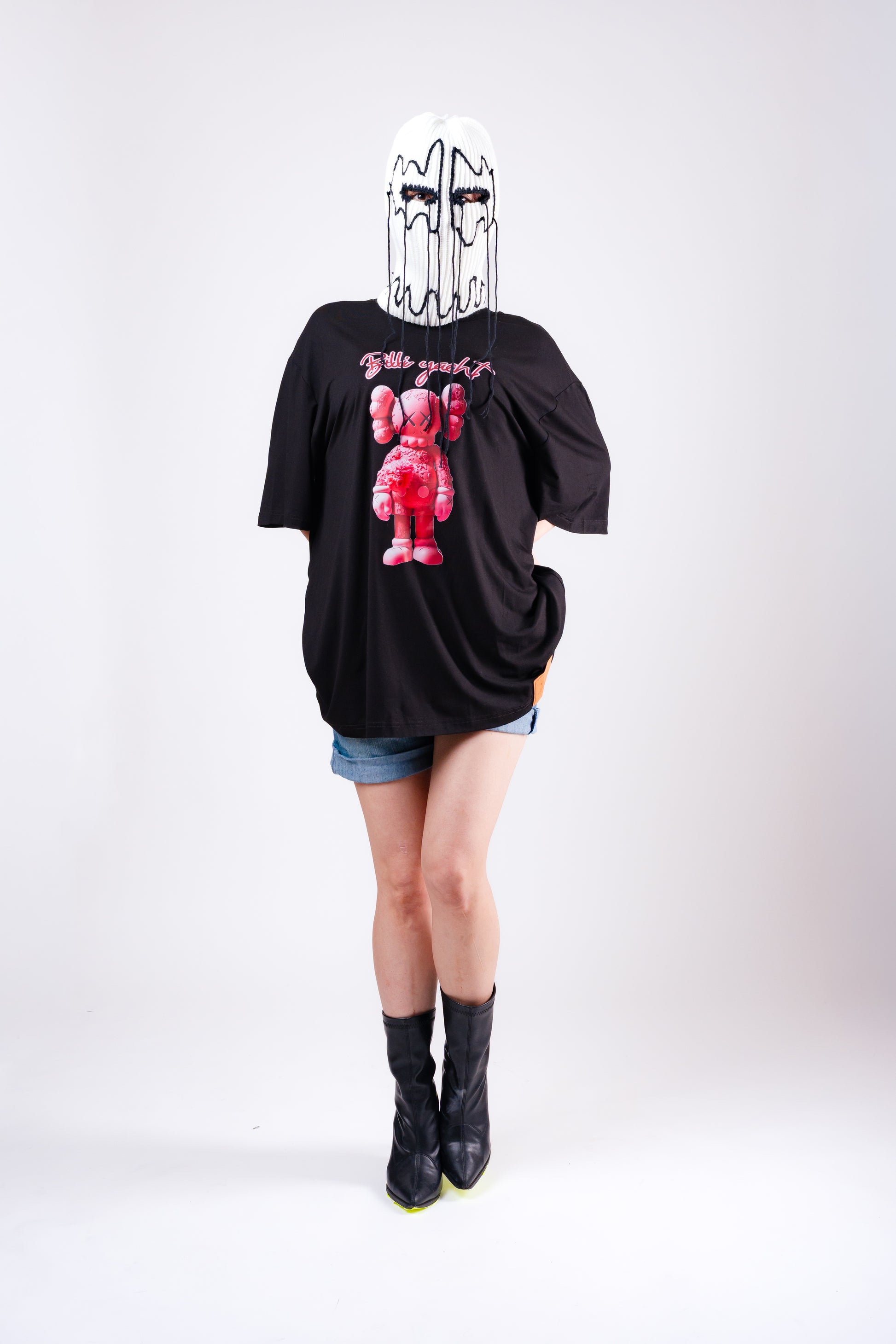 Person wearing a black t-shirt with a graphic design, denim shorts, and black boots on a white background