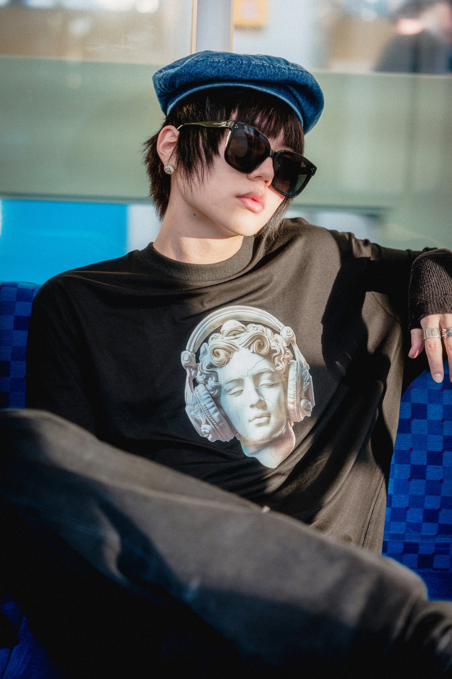 Person wearing a black t-shirt with a graphic design, sunglasses, and a cap in an indoor setting.
