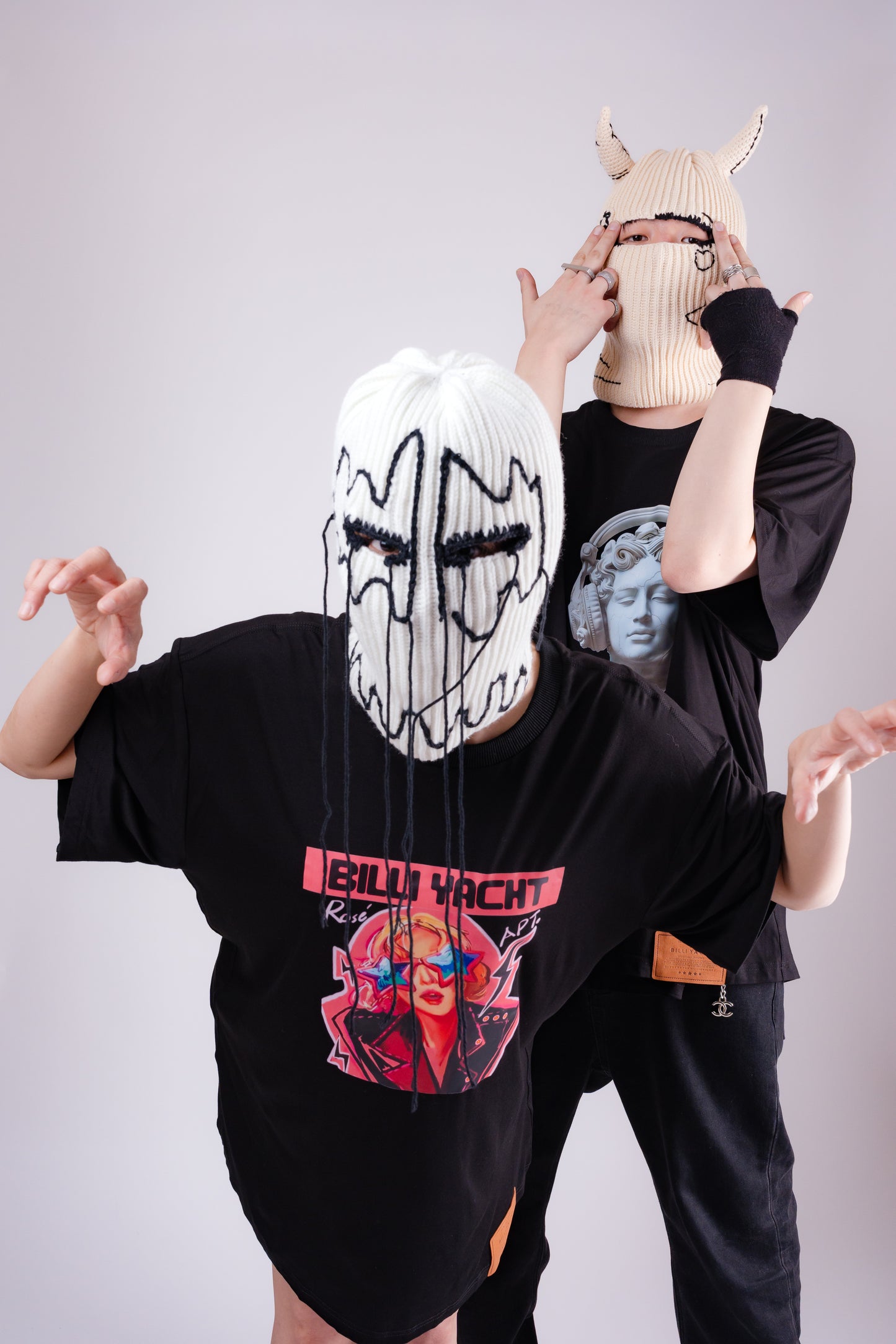 Two people wearing black oversized t-shirts with graphic designs on a plain background