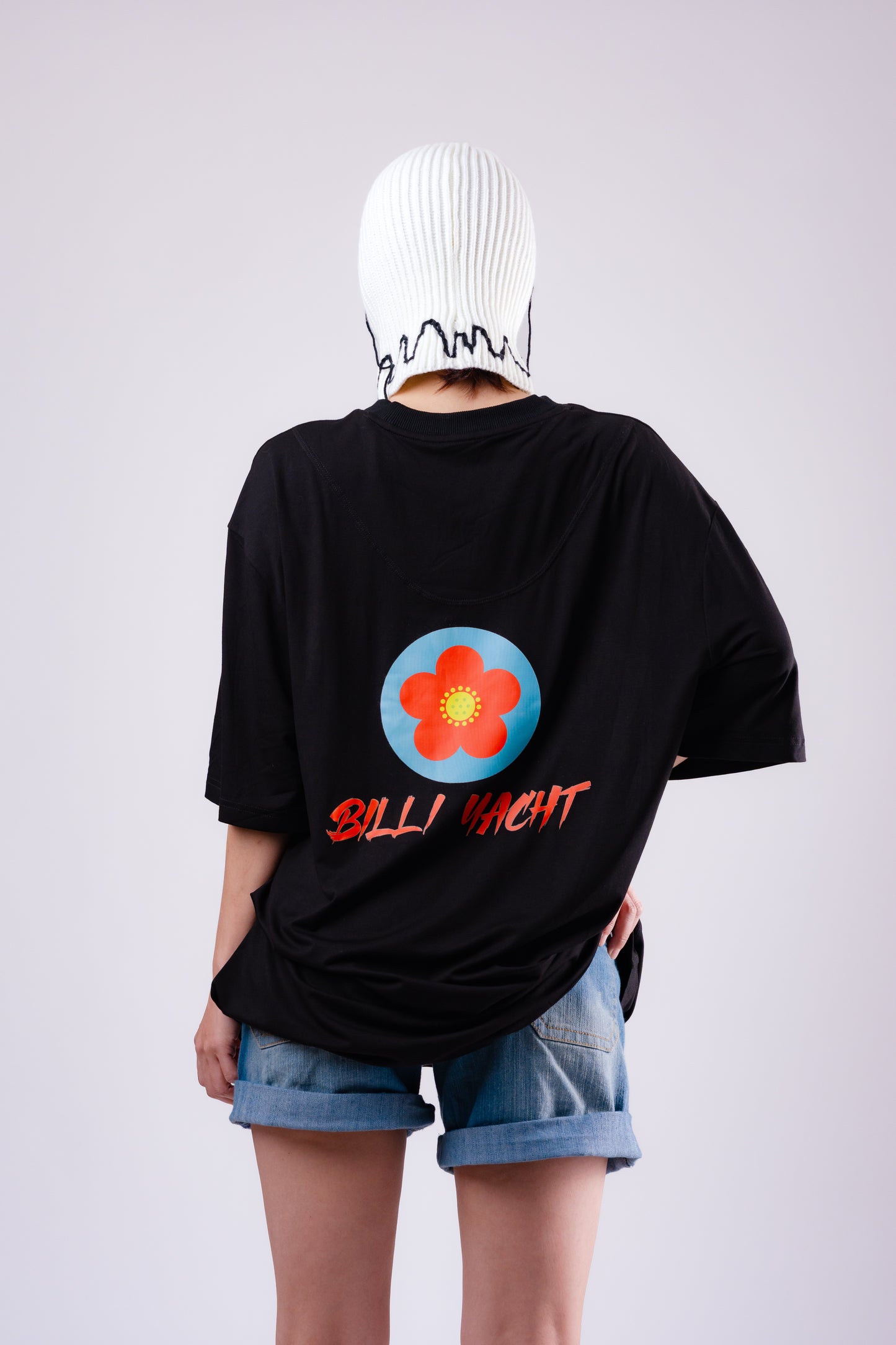 Person wearing a black t-shirt with a colorful flower design and text, standing against a plain background.