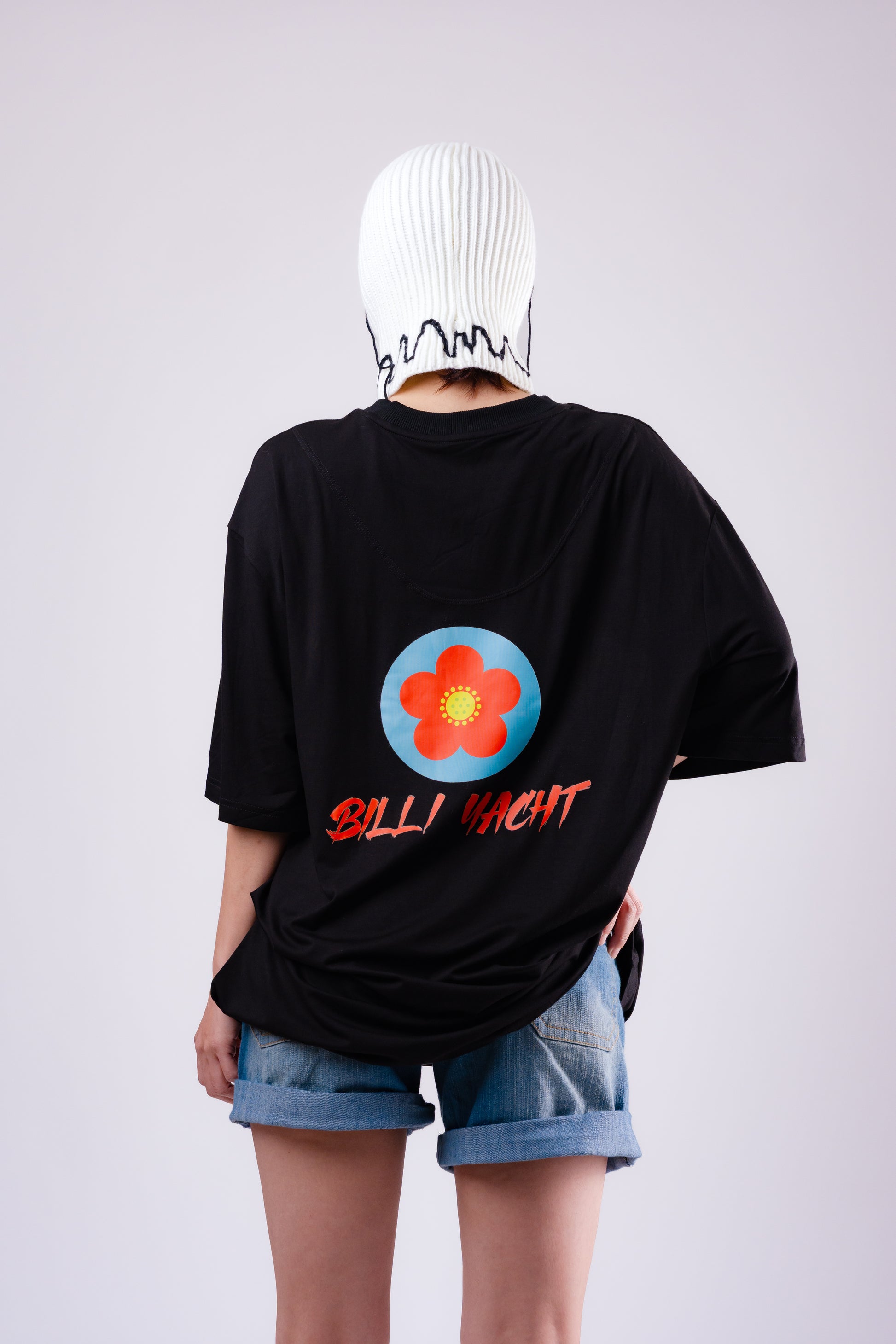 Person wearing a black t-shirt with a colorful flower design and text, standing against a plain background.