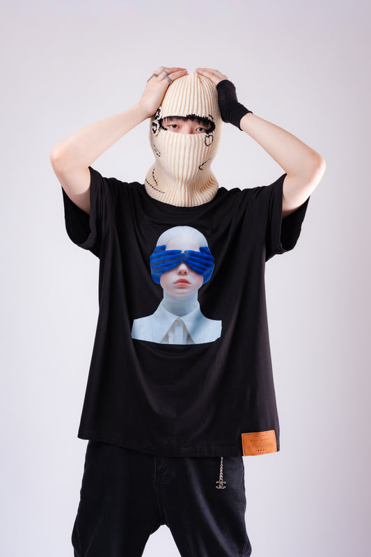 Person wearing a black t-shirt with a graphic design, beige beanie, and dark gloves on a light gray background