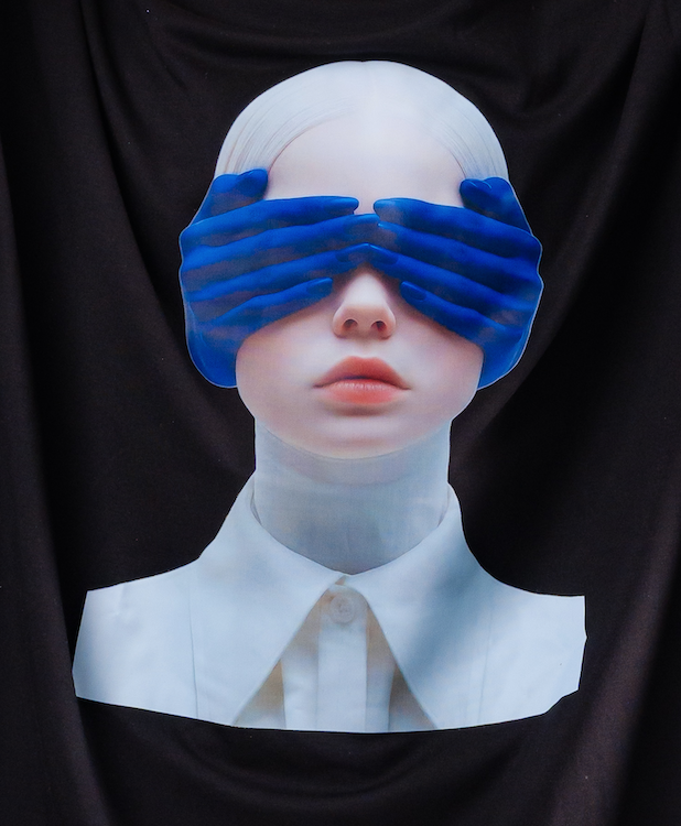 Person wearing a white outfit with blue gloves covering their eyes against a black background