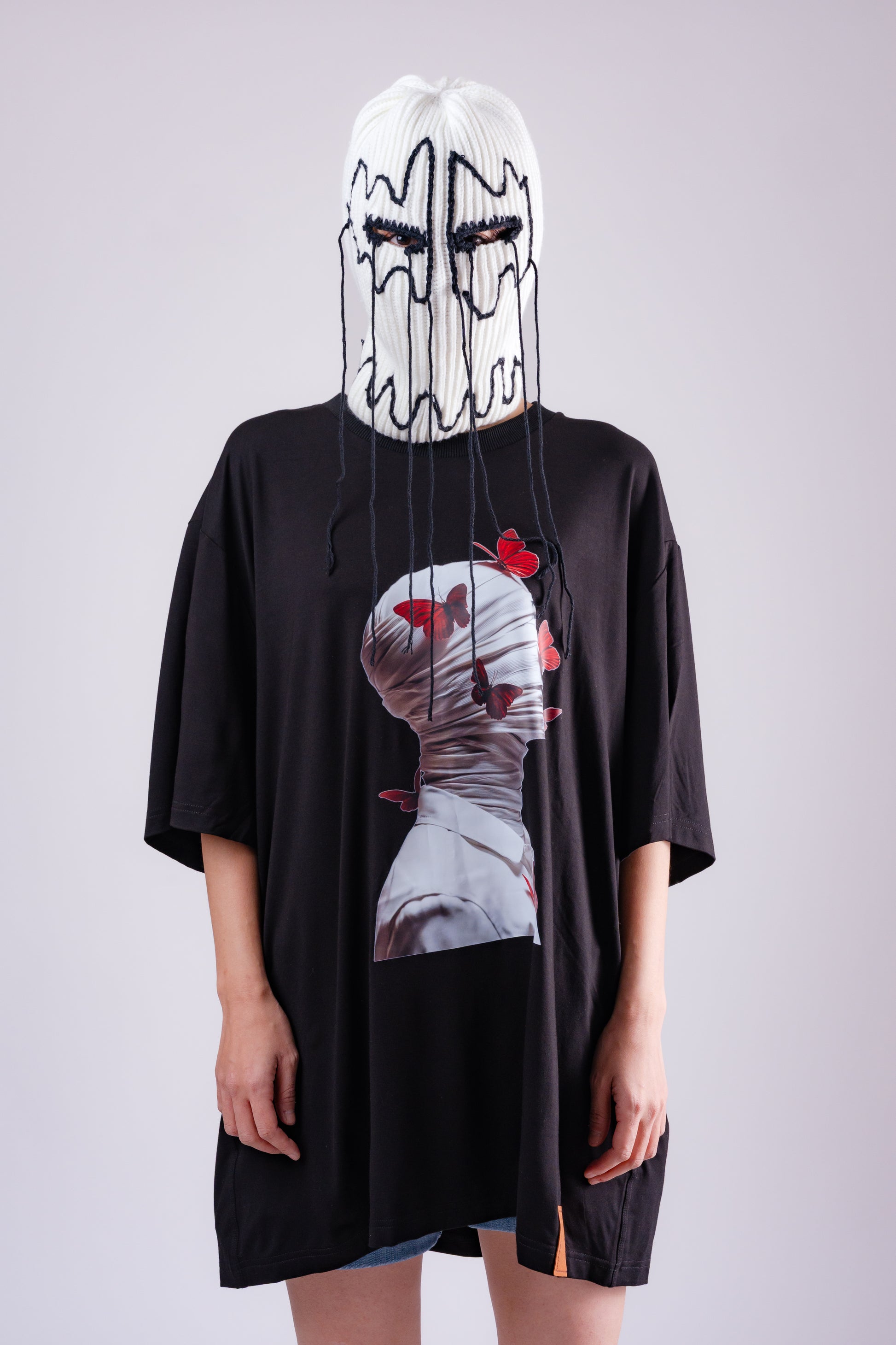 Person wearing a black t-shirt with a graphic design and a white mask with black lines.