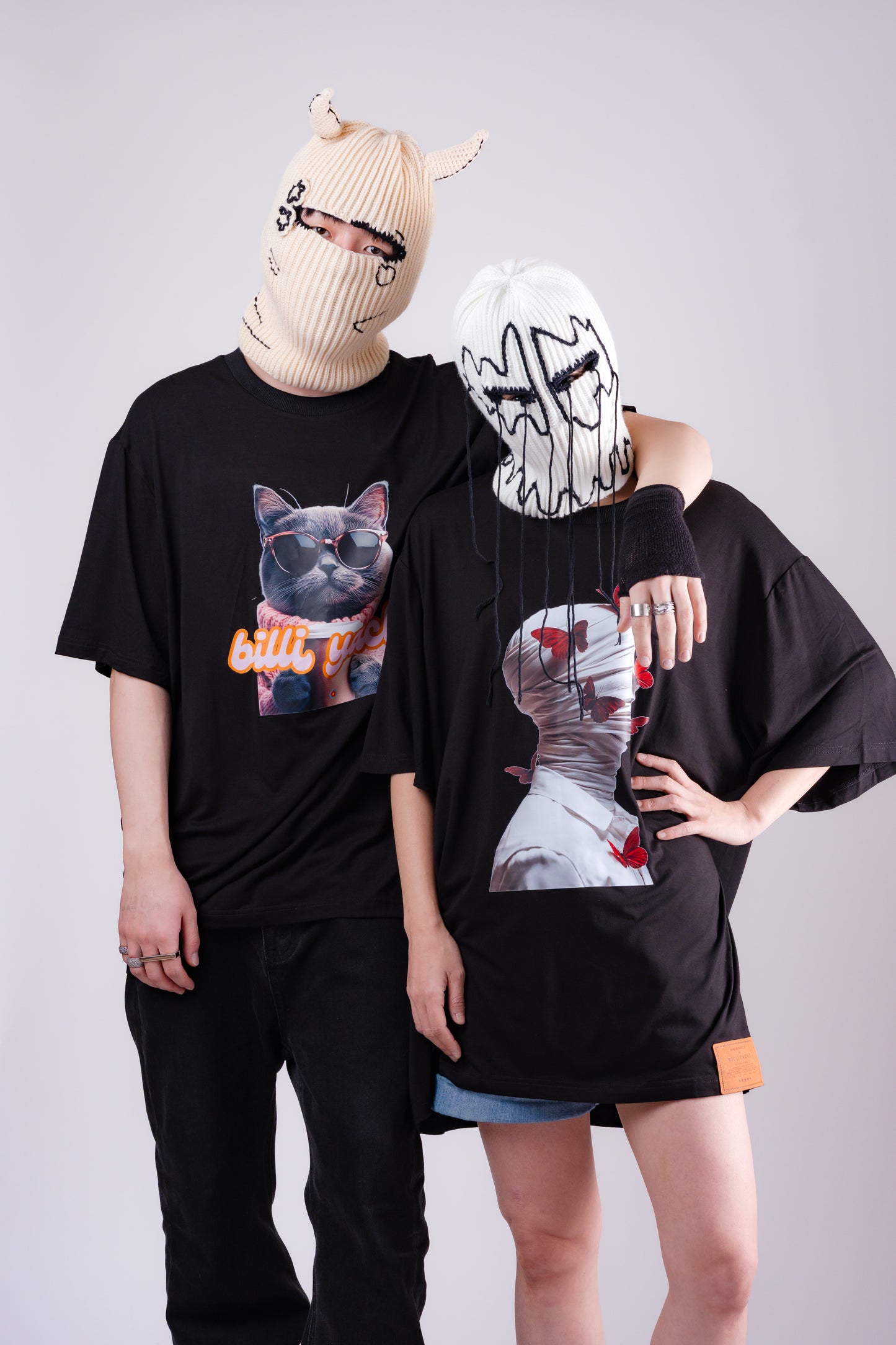 Two people wearing black outfits with graphic designs on a plain background