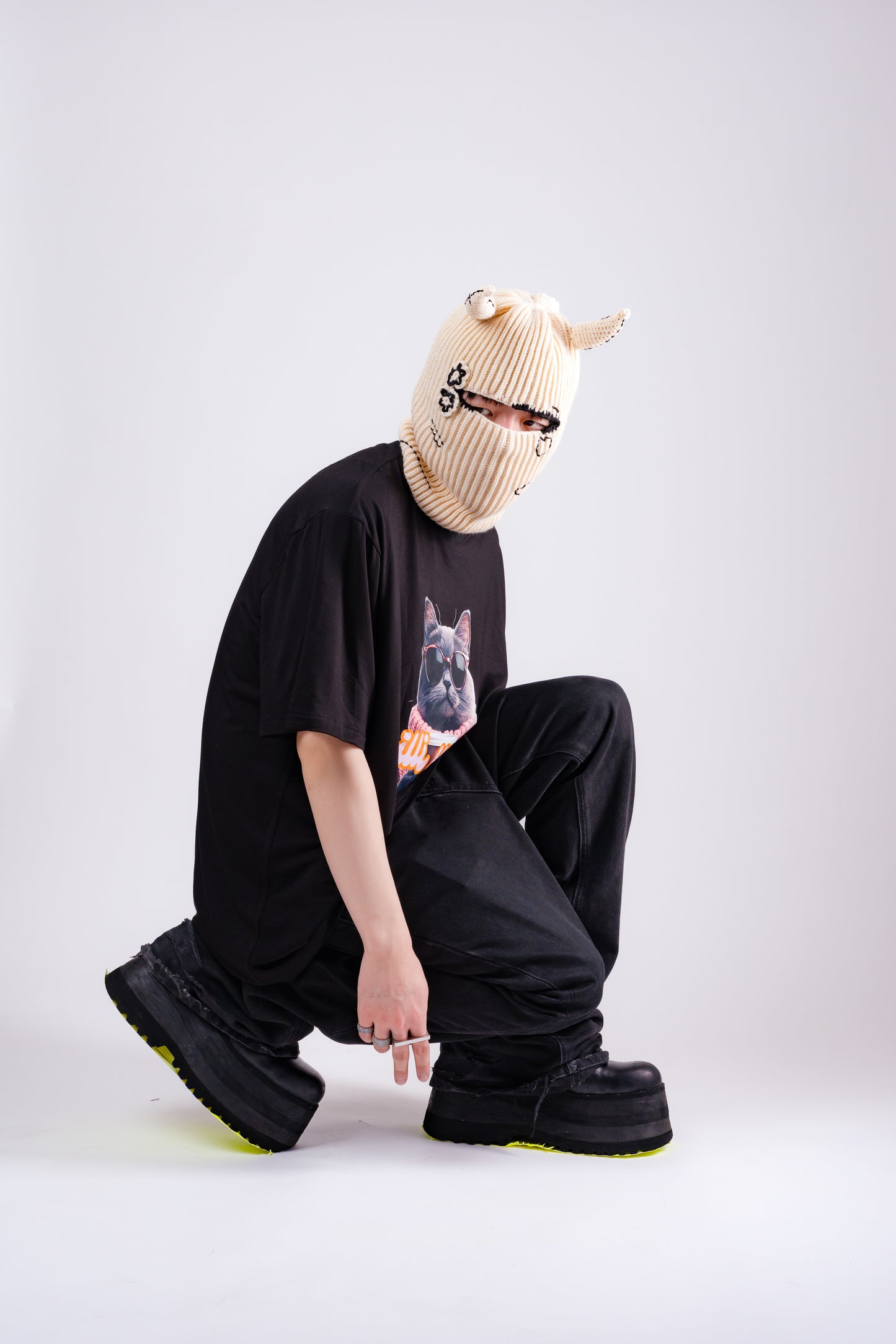 Person wearing a black t-shirt with a graphic design, black pants, and a beige knit hat on a white background.